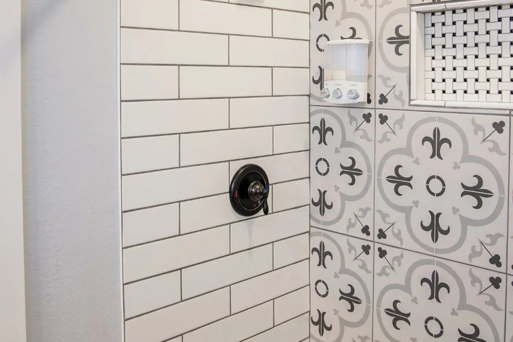 Casa de banho com azulejos brancos, puxador de porta preto e dispensador de toalhas branco.