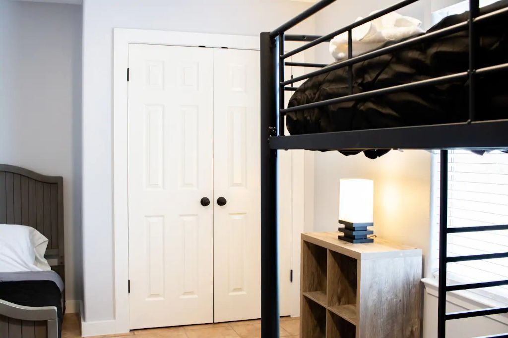 Una cama litera con escritorio y lámpara, una puerta blanca y una silla en una habitación con suelo de baldosas.
