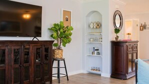 A living room with a flat-screen TV, a large potted plant, a bookshelf, and a cabinet. - Staycation House | Modern and Spacious (Austin)