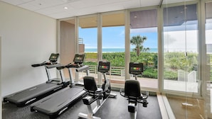 A fitness center with treadmills and elliptical machines, large windows with a view of the outdoors. - Beachfront Condo With Pools, Tennis Courts and gym (Marco Island)