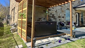Ein Steinhaus mit einer Holzpergola, einem Whirlpool und Sitzgelegenheiten im Freien.