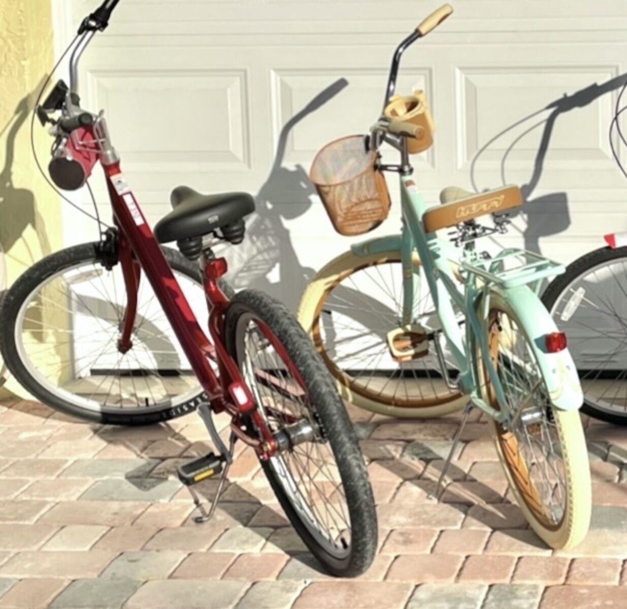 Two bicycles parked on a brick pavement in front of a white garage door.