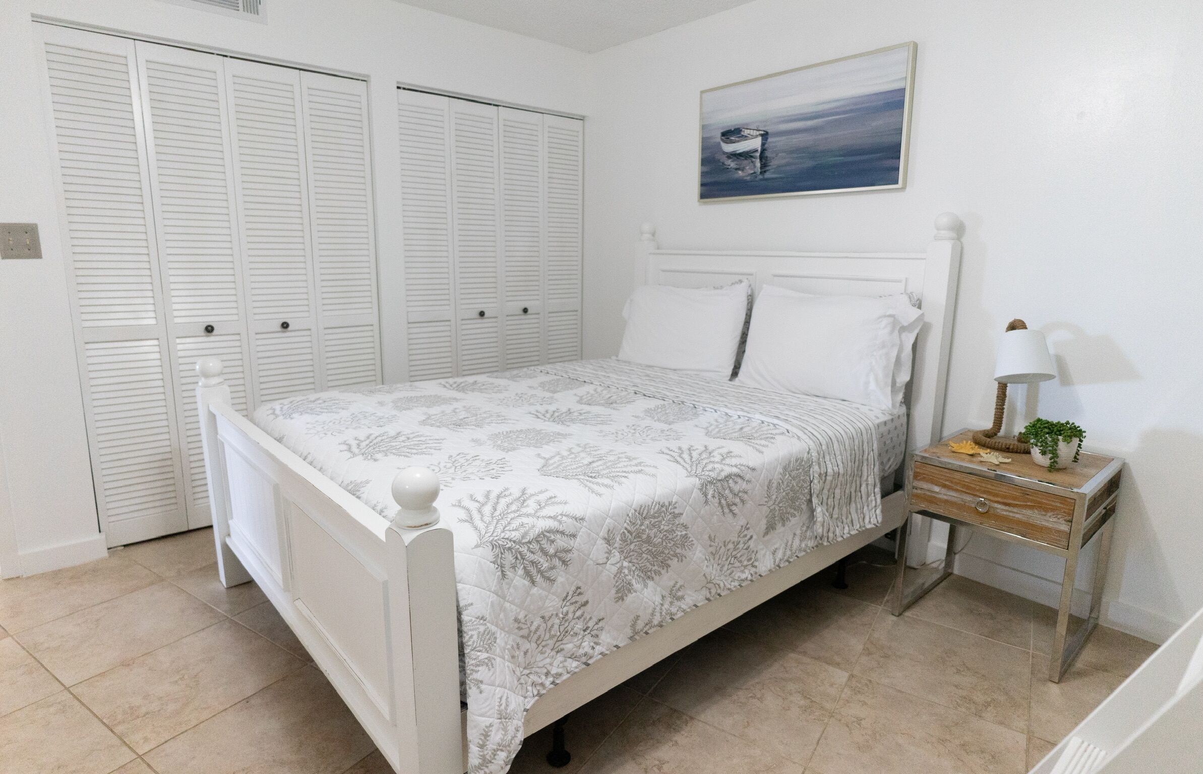Une chambre à coucher avec un lit, une armoire blanche et une table de chevet avec une lampe et une plante.