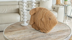 Ett vardagsrum med ett runt soffbord, en beige soffa, en vit lampa och en inramad tavla på väggen.