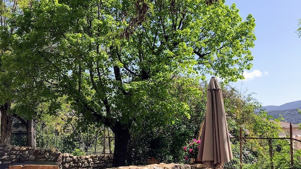 Une terrasse extérieure avec un mur en pierre, une porte en bois et une table ronde entourée de chaises.