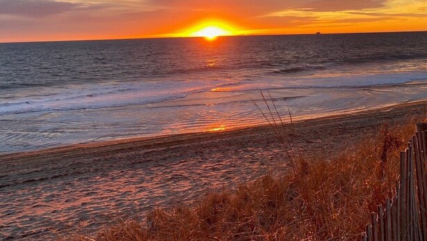 Ein Sonnenuntergang über dem Meer mit einem Strand im Vordergrund.