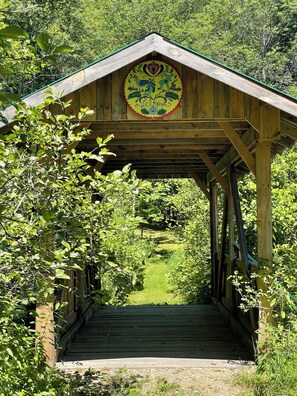 Un pont couvert en bois, agrémenté d’une enseigne décorative, et entouré d’une végétation luxuriante.