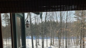 Vista desde una ventana con una terraza de madera cubierta de nieve y una barandilla de metal.