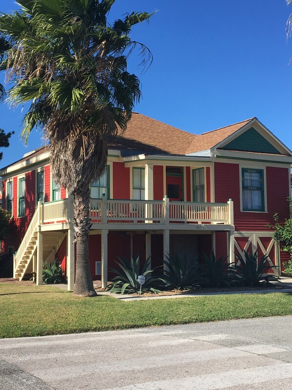 A two-story house with a red exterior, a balcony, and a staircase leading to the second floor. - Cozy Bungalow located 2 blocks from the beach-  (Galveston)