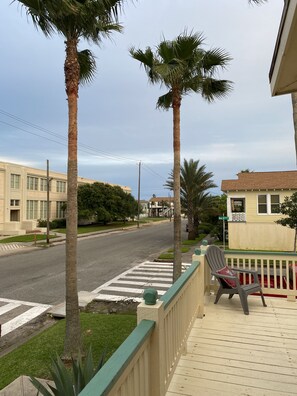 Stroll along the tranquil street lined with palm trees and greenery, passing by a bench for a moment of relaxation.
