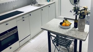 A modern kitchen with white cabinetry, a marble countertop, and a dining area with a table set for two.