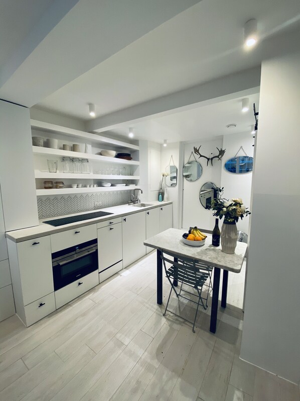A modern kitchen with white cabinetry, a built-in oven, and a dining area with a table and chairs.