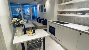 A modern kitchen with white cabinetry, a dining table with a vase of flowers, and a bowl of fruit.