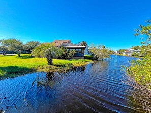 Zona residenziale con una casa vicino a un corso d'acqua tranquillo, immersa nel verde e sotto cieli sereni.