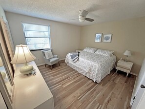 A bedroom with a bed, a chair, a desk with a lamp, a ceiling fan, and a window with blinds. - 3 Sabor de Sal-Seas The Day (St. Augustine)