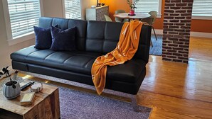 A modern living room with a black leather sofa, a wooden coffee table, and a brick accent wall. - Modern Condo in the West End, central to everything you want to enjoy in P-Town. (Provincetown)