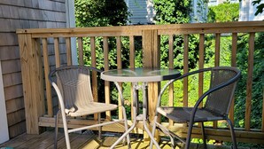 A wooden deck with two wicker chairs and a glass-top table. - Modern Condo in the West End, central to everything you want to enjoy in P-Town. (Provincetown)