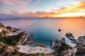 A coastal landscape with rocky formations, clear blue waters, and a distant view of the horizon.