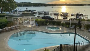 Una piscina con un pabellón, sillas de descanso y vistas a barcos en el agua al atardecer.