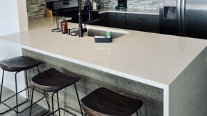 Una cocina moderna con una isla grande, taburetes de bar, electrodomésticos de acero inoxidable e iluminación colgante.