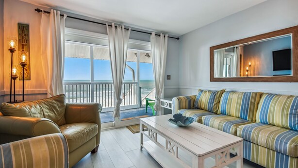 A living room with a sofa, a coffee table, and a view of the ocean through large windows.