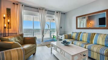 A living room with a sofa, a coffee table, and a view of the ocean through large windows.