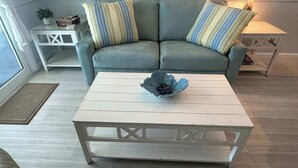 A living room with a grey sofa, striped pillows, a white coffee table with a decorative bowl, and a small white side table with a lamp.