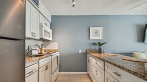 A modern kitchen with white cabinets, a granite countertop, a microwave, and a sink.