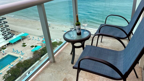 Ein Balkon mit zwei Stühlen, einem Tisch mit einer Flasche und Gläsern sowie Blick auf Strand und Pool.