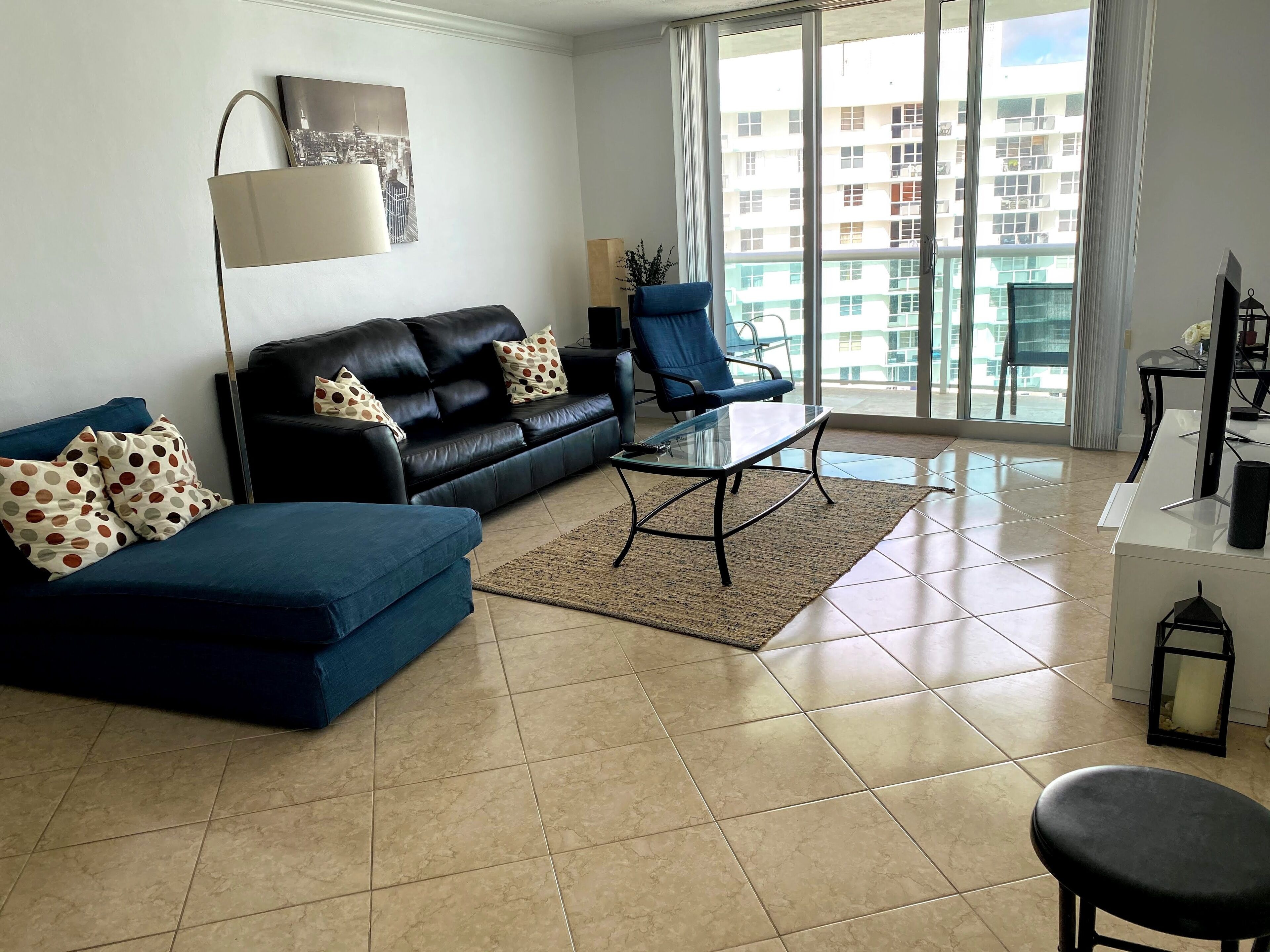 A modern living room with a black leather sofa, blue armchair, and a glass coffee table.