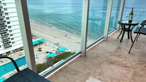 Ein Balkon mit Blick auf einen Strand, ein Pool und ein Tisch mit einer Flasche und Gläsern.