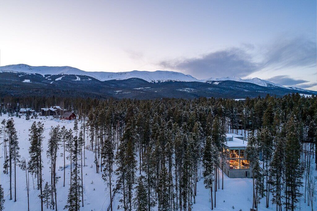 A snow-covered landscape with a lodge surrounded by tall pine trees.