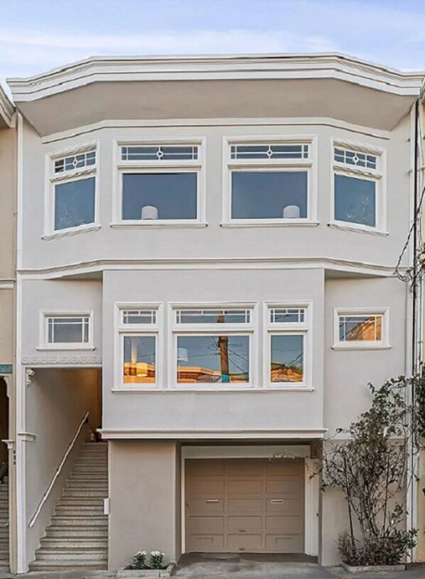 Un edificio de dos plantas con garaje, varias ventanas y una escalera que conduce a la entrada.