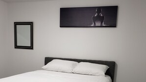 Una cama bien hecha con ropa blanca en una habitación con suelo de madera oscura y paredes blancas.