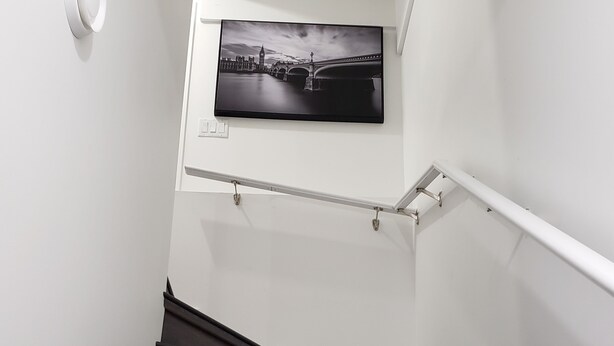 Una escalera con peldaños de madera oscura, paredes blancas y una fotografía blanco y negro de un puente.