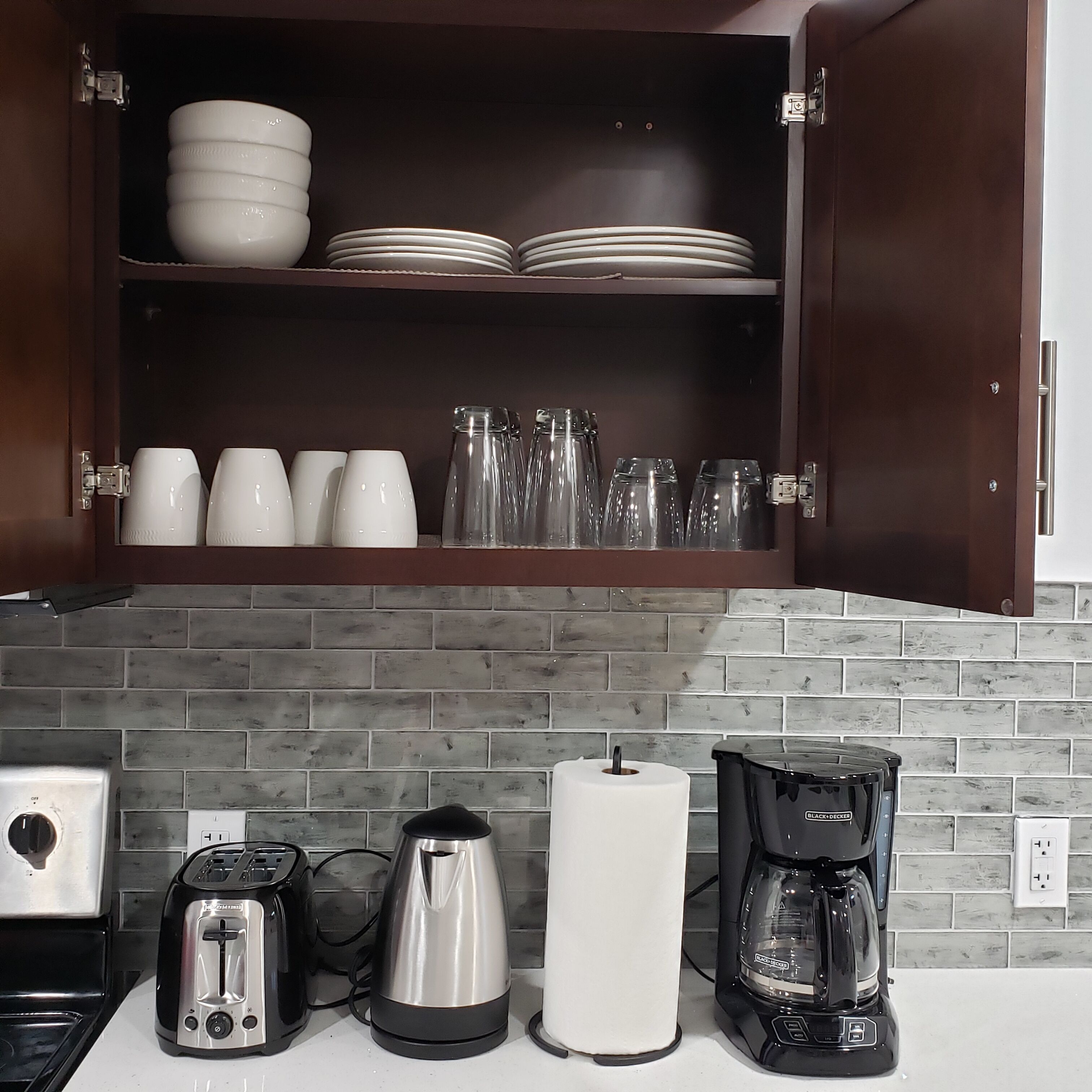 A kitchen with a brick backsplash, a coffee maker, a kettle, a toaster, and a roll of paper towels on the counter.