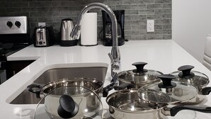 Una cocina con un lavamanos de acero inoxidable, un grifo moderno y varias ollas con tapas.