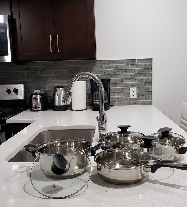 A kitchen with a stainless steel sink, a modern faucet, and several pots with lids.