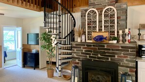 Un vaste salon doté d’une cheminée en pierre, d’un escalier en bois et d’un téléviseur fixé au mur.