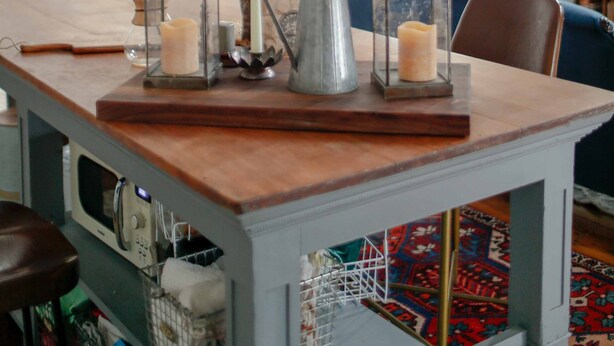 Un coin repas avec une table en bois, des photophores en verre transparent et un vase contenant des plantes séchées.