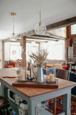 A dining area with a wooden table, clear glass candle holders, and a vase with dried plants.
