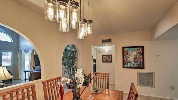 A dining area with a wooden table, chairs, a vase with flowers, and a modern chandelier. - Central Tucson Gated Retreat (Tucson)