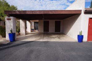 A covered parking area with a concrete floor, two blue planters with cacti, and a red door on the right.