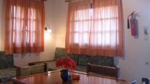 A dining area with a wooden table and chairs, a vase with flowers, and a ceiling fan. - Androulakis Apartments (Platanias)