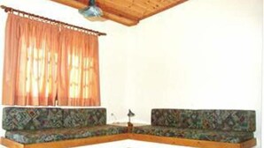A corner room with a wooden ceiling, a patterned sofa, and a window with orange curtains. - Androulakis Apartments (Platanias)