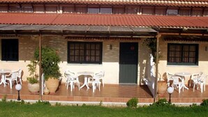 A building with a tiled roof and a covered patio area with white chairs and tables. - Androulakis Apartments (Platanias)