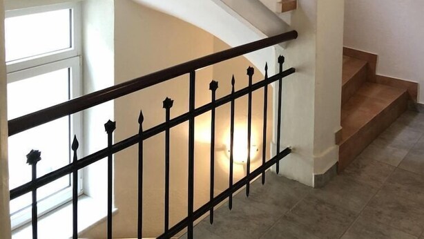 A staircase with a black metal railing and wooden steps, leading to a landing with a white wall and a window. - Wildbach City Apartments (Zell am See)