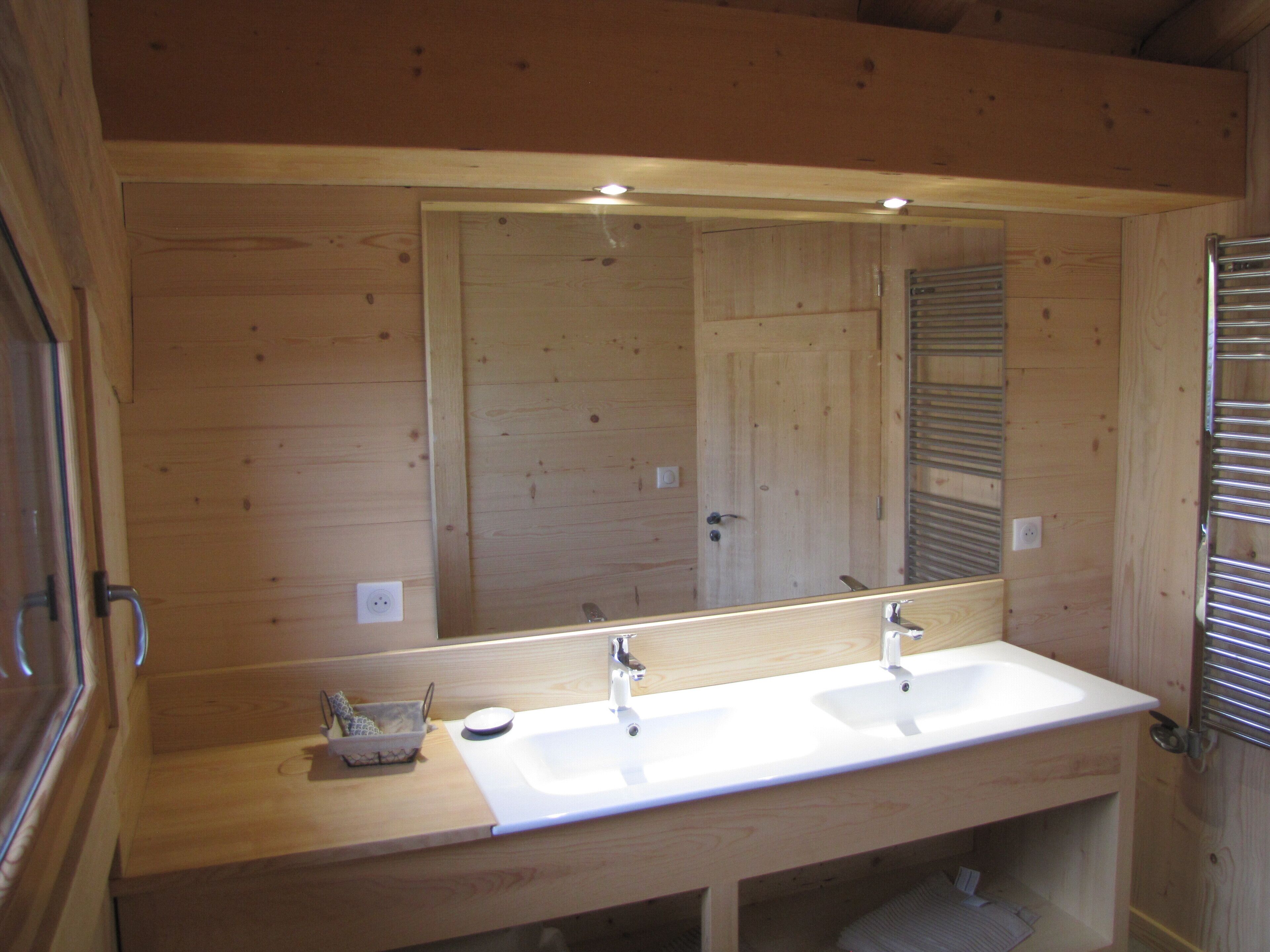 A wooden cabin bathroom with a large mirror, two sinks, and a towel rack.