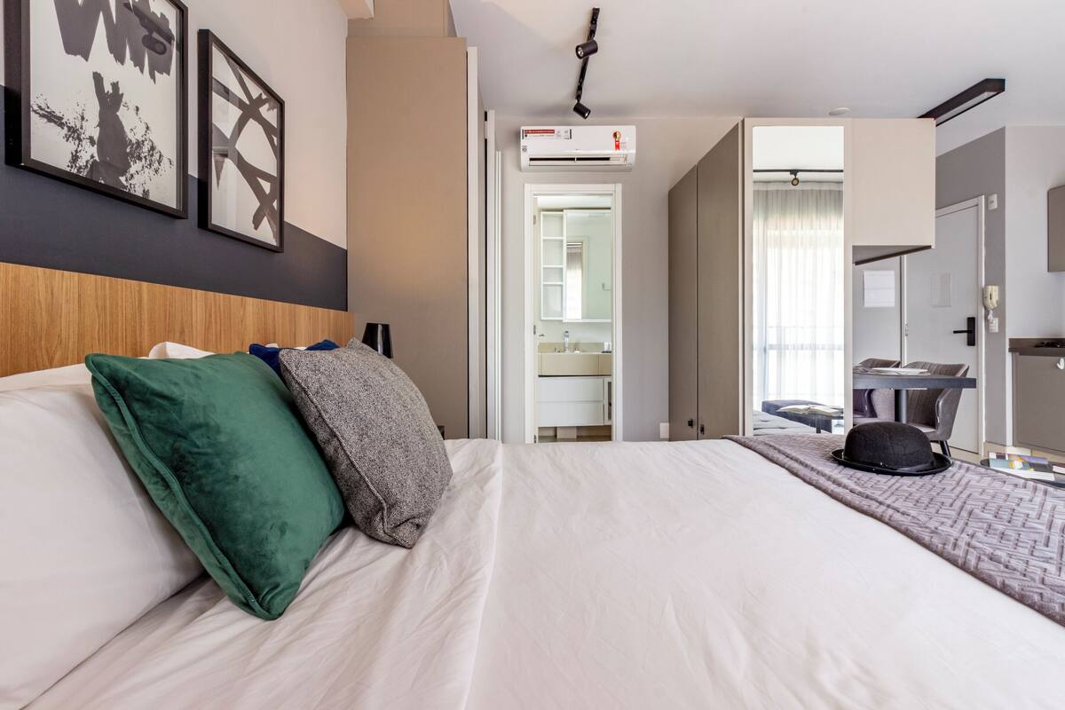A hotel room with a bed, pillows, a hat on the bed, and a door leading to a bathroom.