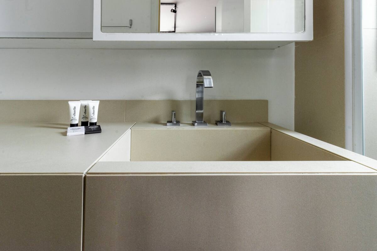 A modern bathroom with a white countertop, a sink with a single faucet, and three tubes of lotion on the counter.